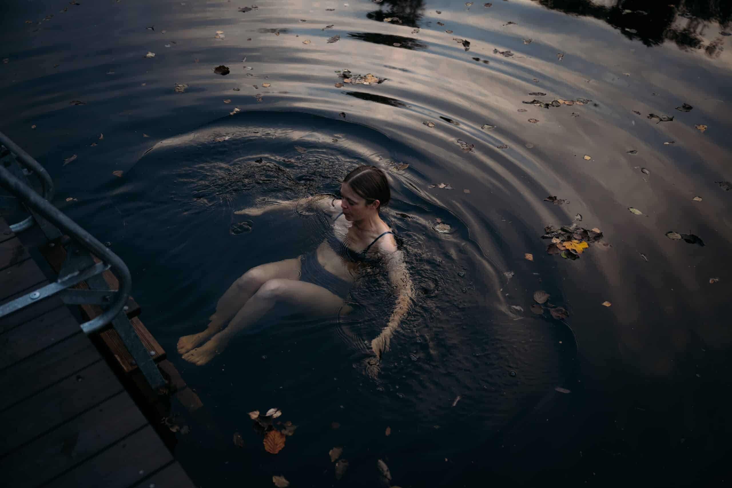 a woman in a swimsuit dipping in dark water with autumn leaves